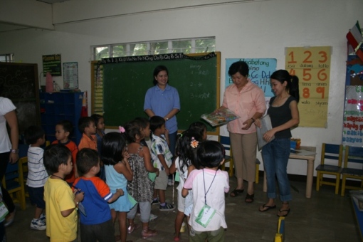 Ms. Mely Villanueva (wearing pink) and Ms. Isa Saplala (wearing a blue blouse) distributing story books to the CHEERS preschool children. 